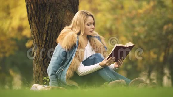 时尚的女士在中央公园阅读冒险书坐在树下秋天视频的预览图