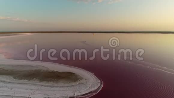 日落时分一名男子在一个美丽的粉红色湖泊中进行风筝冲浪全景视频的预览图