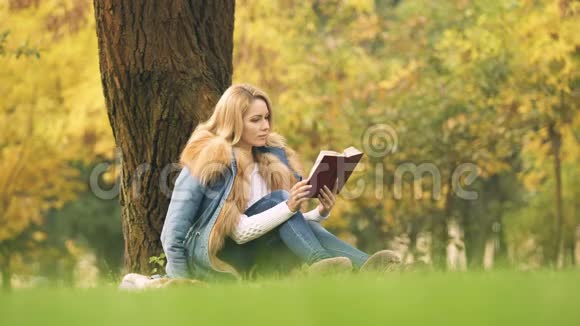 漂亮的女人看有趣的书坐在树下消磨闲暇时间视频的预览图