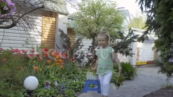 小女孩拿着一篮子花玩具和椅子走在房子附近的小路上视频的预览图