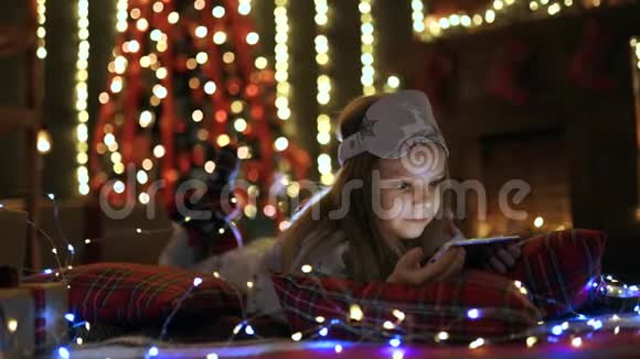 在圣诞树附近玩平板电脑智能手机的女孩视频的预览图