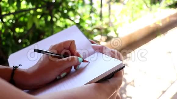 女人在阳台上的笔记本上写字女性在日记特写上做笔记视频的预览图