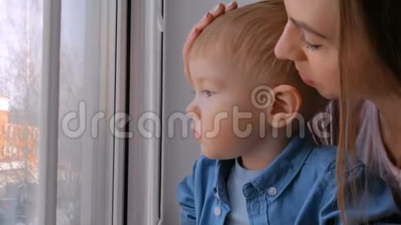 年轻的母亲和忧郁的小男孩透过窗户视频的预览图