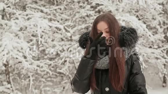 年轻迷人的女孩穿着温暖的冬季衣服摆在白雪覆盖的杉树附近微笑的女孩快乐的降雪视频的预览图
