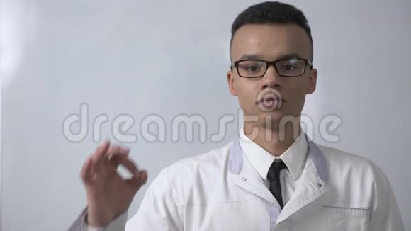 年轻成功的非洲科学家穿着白色外套和眼镜露出OK标志看着相机肖像概念视频的预览图