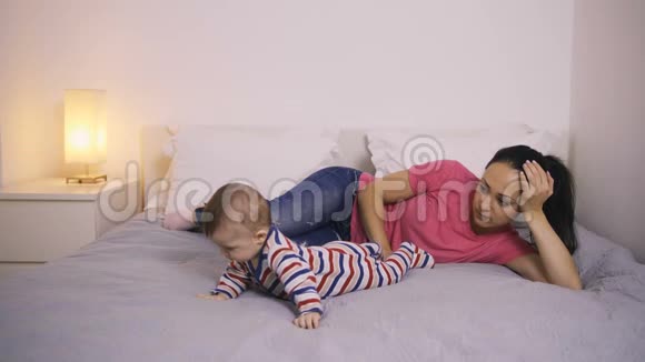 疲惫的母亲躺在床上看着她的孩子视频的预览图