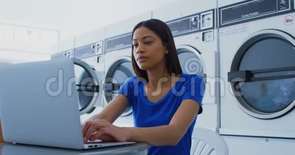 女士在自助洗衣店使用笔记本电脑视频的预览图
