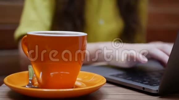 女人在笔记本电脑上工作桌子上放着一杯咖啡远处的咖啡馆工作自由职业概念4k视频的预览图