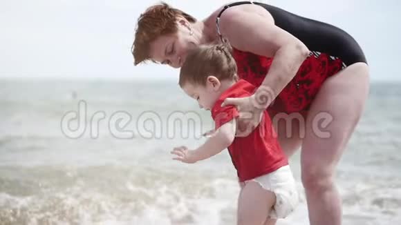 快乐的孩子和奶奶在海边玩耍小男孩开心地笑着笑着在海浪上跳跃视频的预览图