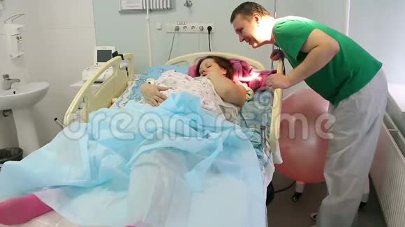 一位年轻的母亲和一位新生儿躺在产房里分娩后放松幸福的父亲吻她视频的预览图