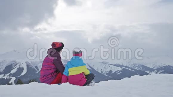 母亲和女儿享受旅程在滑雪场穿着冬装的幸福家庭冬天的时候看着视频的预览图