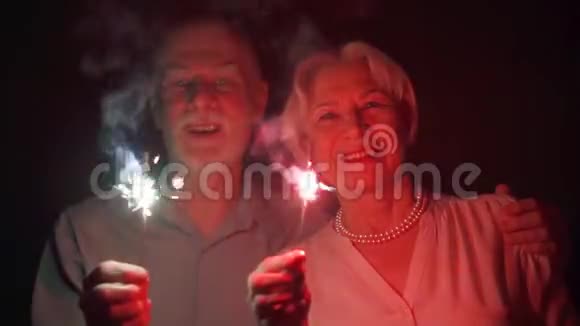 慢动作一对爱炫耀的老夫妇庆祝圣诞节幸福的家庭手持孟加拉灯视频的预览图