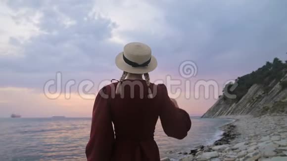 从后面看到的慢动作画一个穿着红色连衣裙和海边草帽的年轻女孩的肖像一个女孩视频的预览图