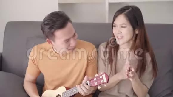 亚洲夫妇在家里的客厅里一起弹吉他和唱歌视频的预览图