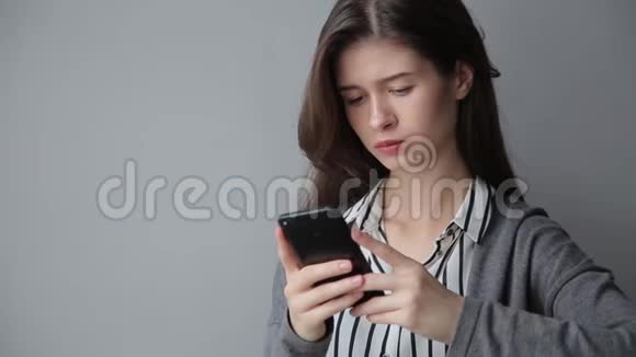 办公室里漂亮的美女在智能手机上发短信灰色背景视频的预览图