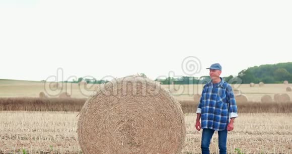 微笑的农夫在农场里翻滚干草打手势视频的预览图
