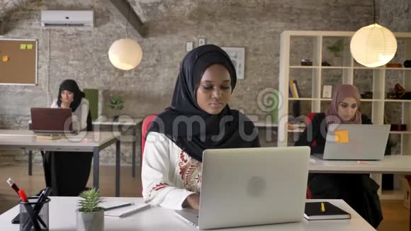 年轻的黑人穆斯林妇女戴着头巾在笔记本电脑上工作打着哈欠昏昏欲睡三个美丽的穆斯林妇女坐在现代视频的预览图