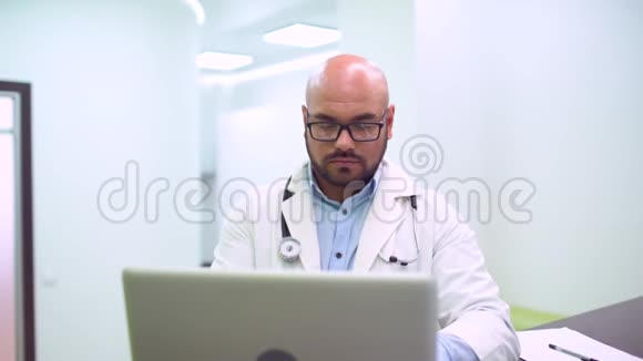 严肃的医生在明亮的办公室里看着笔记本电脑视频的预览图