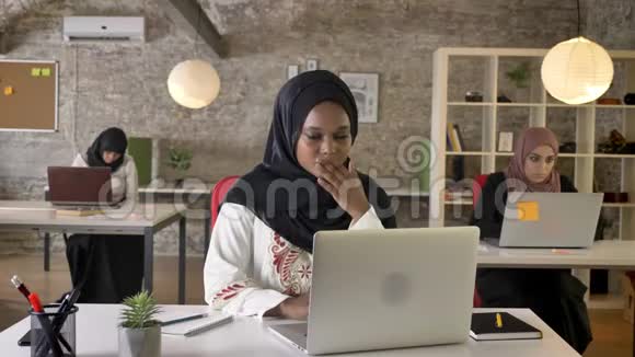 年轻的穆斯林黑人妇女戴着头巾手提电脑工作打哈欠疲惫三个美丽的穆斯林妇女坐在现代视频的预览图