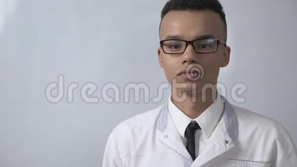 年轻成功的非洲科学家穿着白色的实验室外套和眼镜咬着苹果吃东西看着相机视频的预览图
