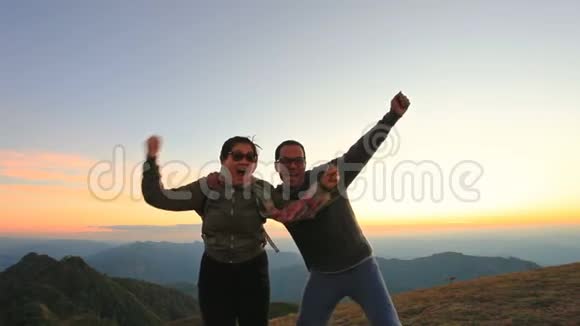快乐的亚洲男人和女人在山顶上放松美丽的日落天空视频的预览图