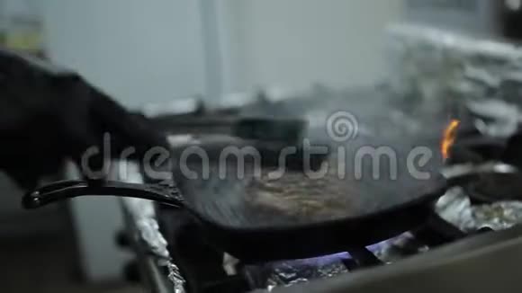 一个厨师在一家餐馆的厨房里用热的烤炉和牛排煎厨师把牛排翻过来视频的预览图