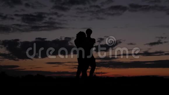 浪漫情侣的黑暗剪影在日落时手挽手旋转视频的预览图