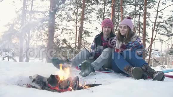 一对穿着冬装的年轻人在一片白雪覆盖的森林里把棉花木桩上煎棉花糖视频的预览图