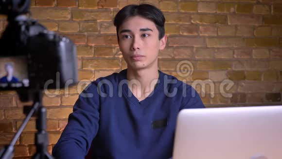 年轻的韩国男性博客写手在镜头下说话在室内做手势的特写照片视频的预览图
