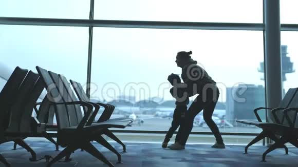 顽皮的母亲抚养她的儿子抱着他在机场透过窗户看充满爱的家人在等待航班视频的预览图