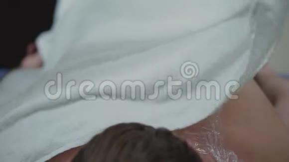 后面的水疗面膜用塑料布和毛巾覆盖的口罩将男性背部封闭起来水疗程序视频的预览图