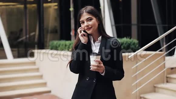 开朗的年轻商务女性站在办公室中心附近在智能手机上交谈她看着摄像机视频的预览图