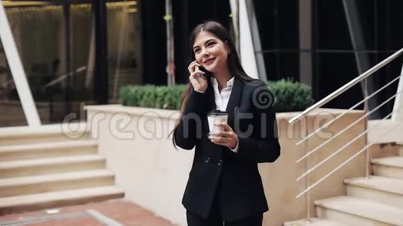 开朗的年轻商务女性站在办公室中心附近在智能手机上交谈她看着摄像机视频的预览图