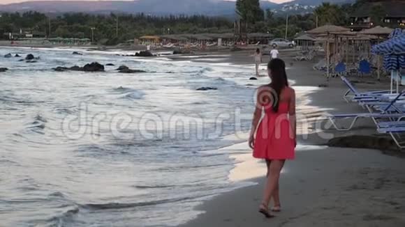 日落时分穿着红裙子在海滩上散步的女人视频的预览图