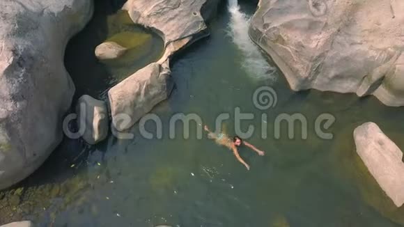 年轻女子在清澈的水中游山河空中拍摄来自飞行无人机快乐的女人飘进来视频的预览图