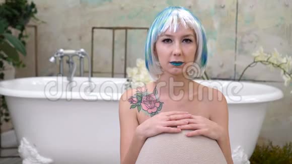 无感情的女人的肖像带着蓝色的嘴唇和假发在浴缸的背景上看着相机视频的预览图