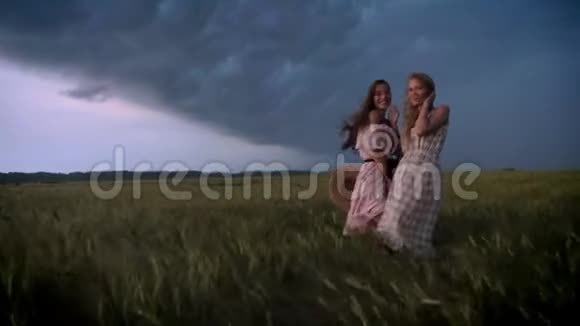 两个穿着裙子的年轻迷人的女孩在夏天的雨天里在田野里发出闪电自由的概念视频的预览图
