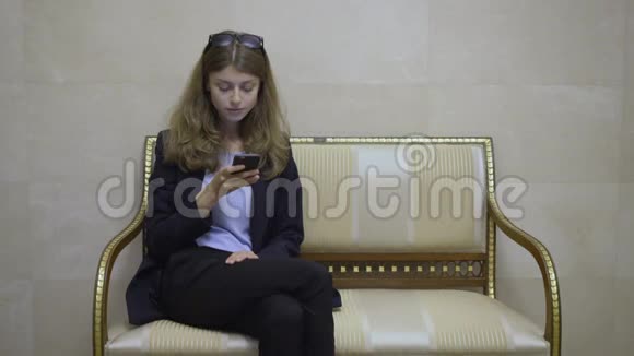 酒店大堂的年轻女商人看着她的智能手机屏幕视频的预览图