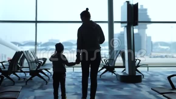 母亲牵着儿子的手他们透过机场的窗户看着飞机充满爱的家人在等待航班视频的预览图