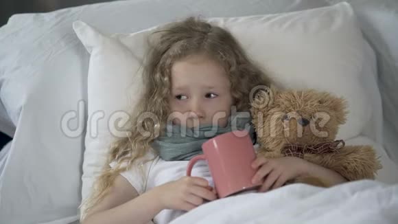 生病的孩子躺在床上杯子里放着热饮料生病的女孩因喉咙疼痛而哭泣视频的预览图