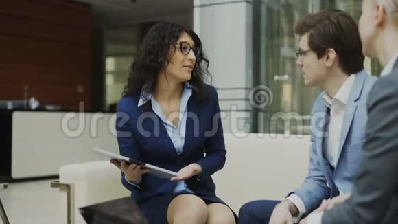 戴眼镜的女商人与坐在现代办公室沙发上的商业伙伴谈未来的合同视频的预览图
