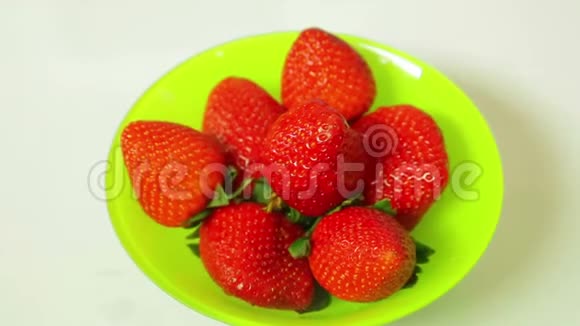 蓝色背景的绿色盘子里的红色新鲜草莓浆果在一个圆圈中旋转视频的预览图