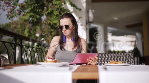 女孩在小酒馆里吃早餐在街头餐馆里用平板电脑浏览互联网视频的预览图