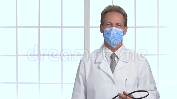 戴防护面罩的微笑医生在他脖子上戴上听诊器视频的预览图