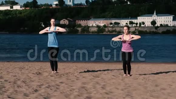 两个女人在城市河边的沙滩上做瑜伽日出时美丽的城市景色特里科纳桑乌蒂哈的姿势视频的预览图