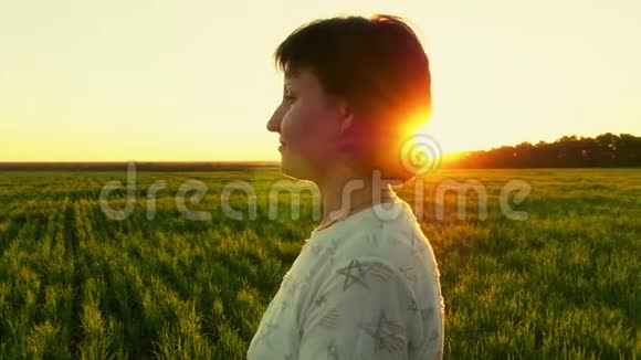 落日背景下年轻女子站在绿色草坪上的肖像视频的预览图