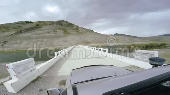 汽车旅行SUV骑在一条河上的白桥上的高山公路上POV车辆行驶的视角视频的预览图