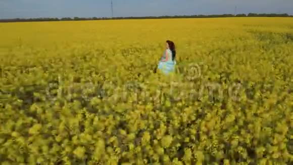 一个穿着蓝色裙子的漂亮女人穿着黄色的田野开着油菜花视频的预览图
