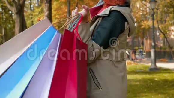 一个长着狐假虎威的女孩在公园里散步用多种颜色的纸袋购物视频的预览图