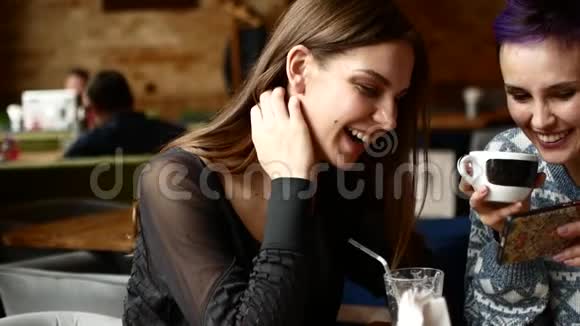 两个朋友在咖啡馆里看智能手机上的视频笑了起来女人在咖啡屋喝咖啡视频的预览图